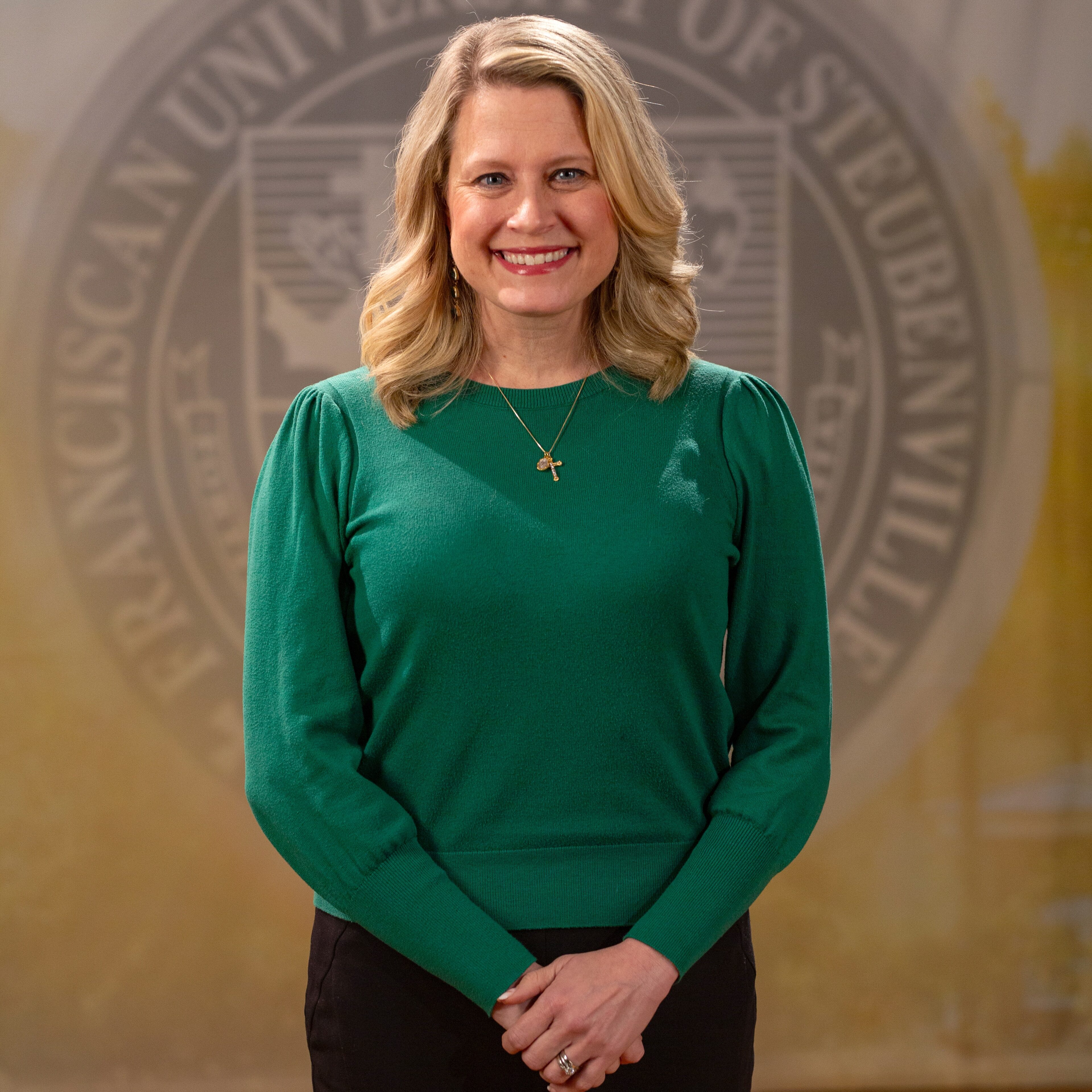 Faculty portrait of Dr. Rebecca Rook standing in front of the Franciscan University of Steubenville seal.