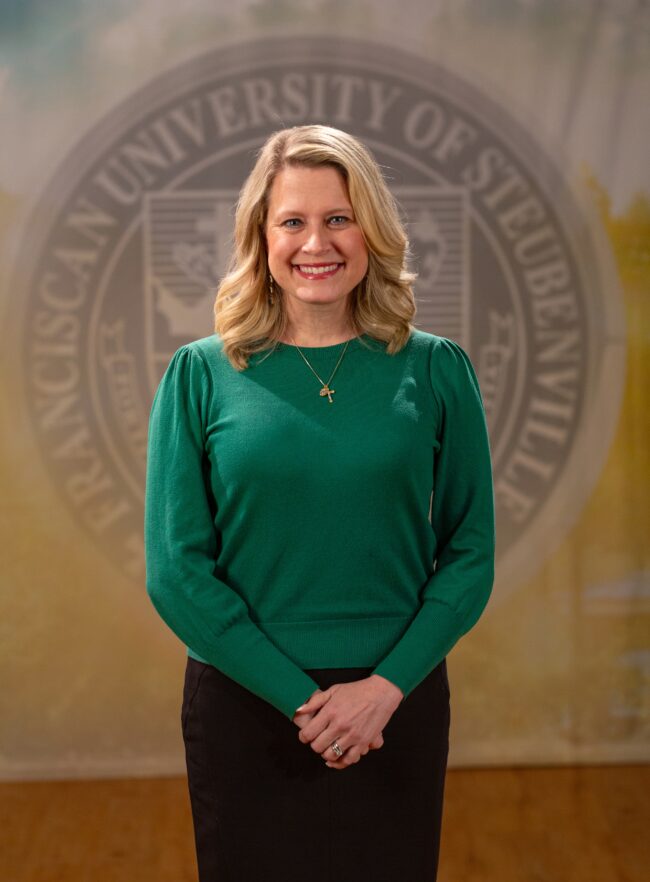 Dr_Rebecca Rook_Faculty Portrait_Spring2026_-2772* Faculty portrait of Dr. Rebecca Rook standing in front of the Franciscan University of Steubenville seal.