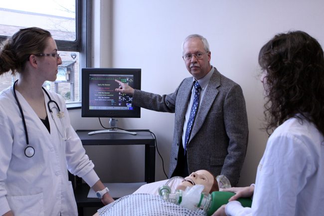 Professor Antinone teaching two students over nursing dummy
