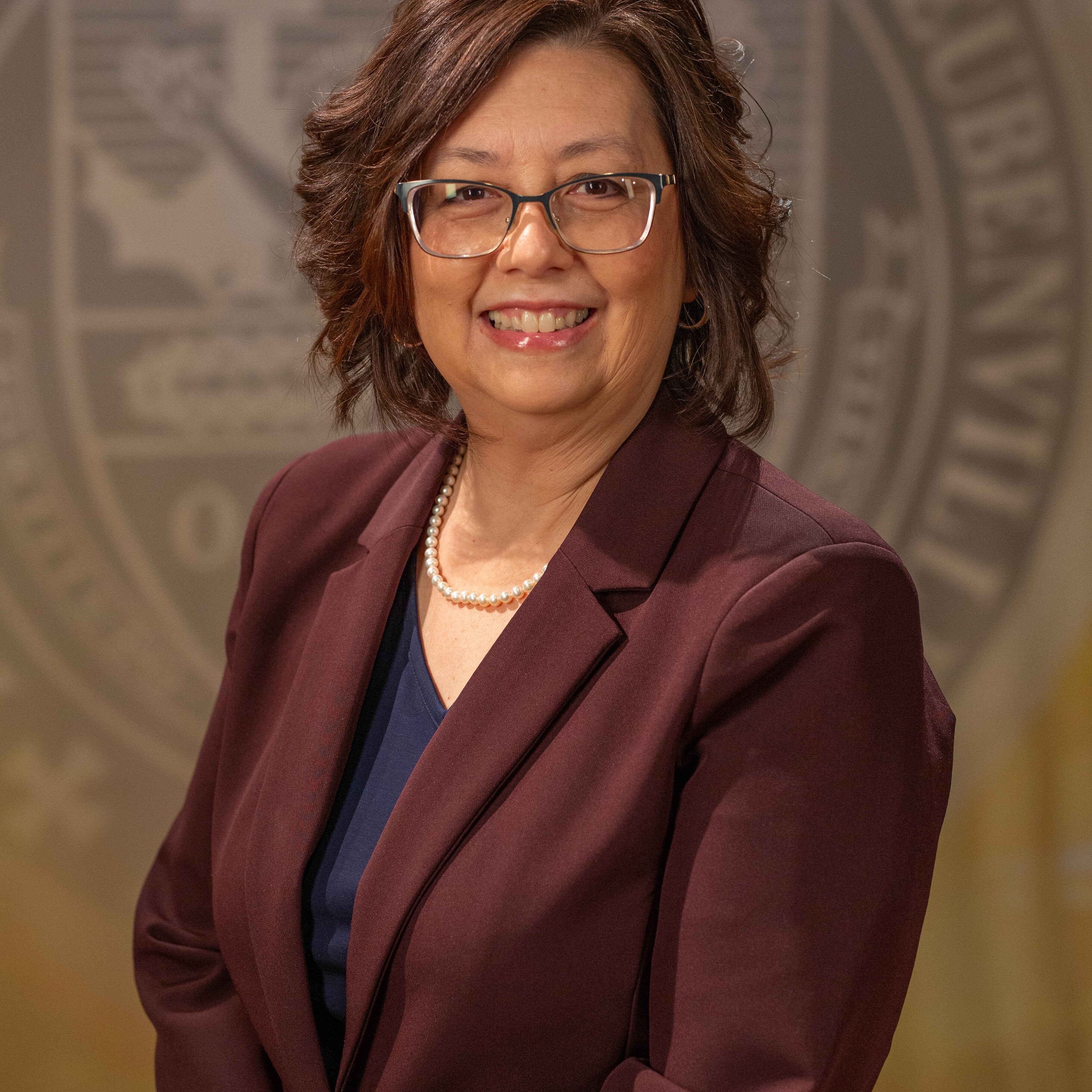 Faculty portrait of a Dr. Diann Schmitt standing in front of the Franciscan University of Steubenville seal.