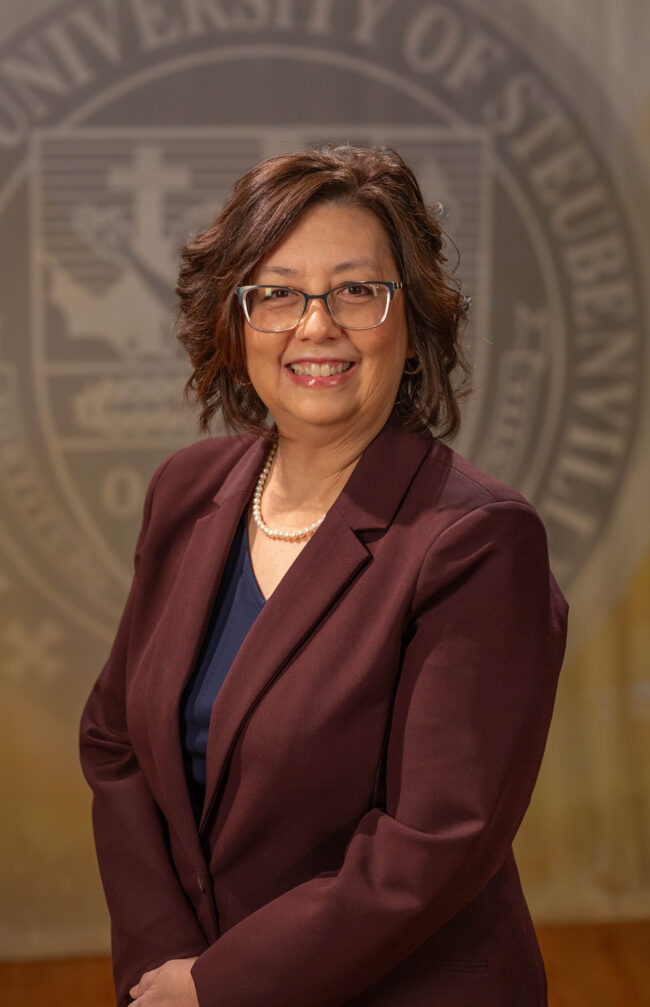 Faculty portrait of a Dr. Diann Schmitt standing in front of the Franciscan University of Steubenville seal.