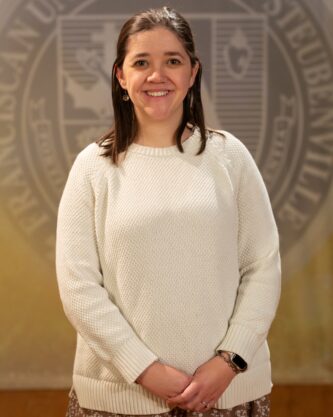 Katherine Holler_Faculty Portrait_Spring2026_-2867 Faculty portrait of a Dr. Katherine Holler standing in front of the Franciscan University of Steubenville seal.