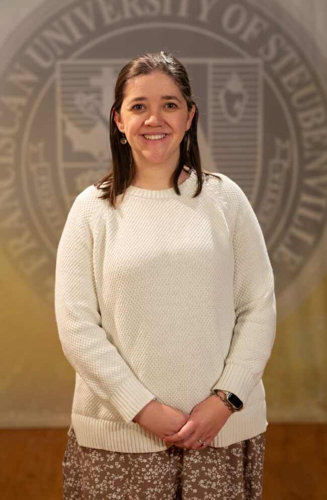 Faculty portrait of a Dr. Katherine Holler standing in front of the Franciscan University of Steubenville seal.