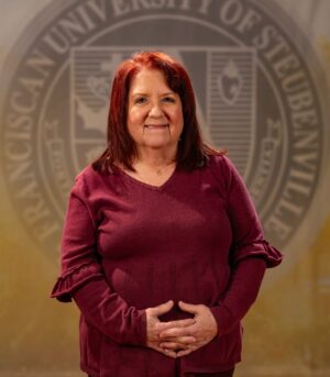 Faculty portrait of Dr. Kimberley Donnelly standing in front of the Franciscan University of Steubenville seal.