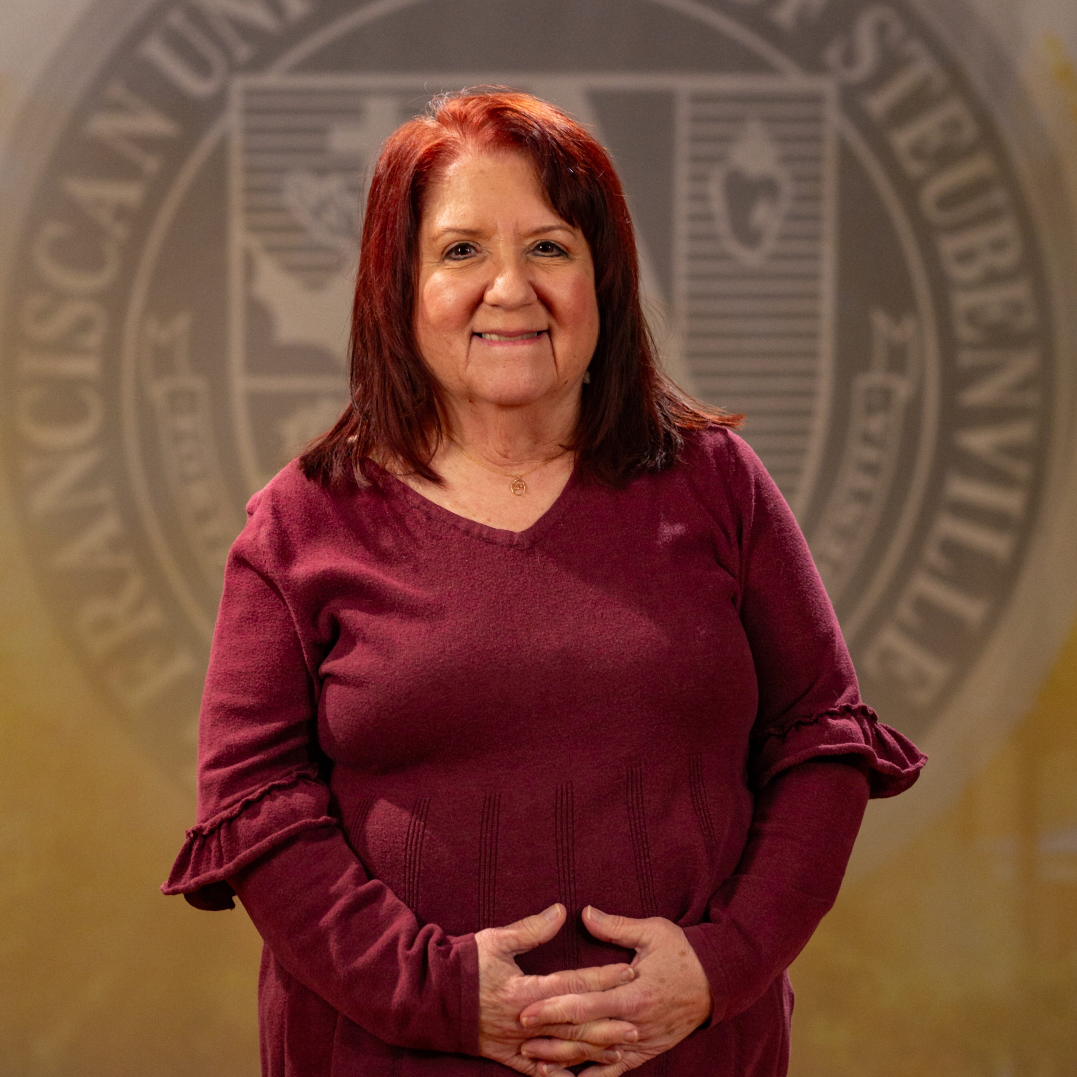 Faculty portrait of Dr. Kimberley Donnelly standing in front of the Franciscan University of Steubenville seal.
