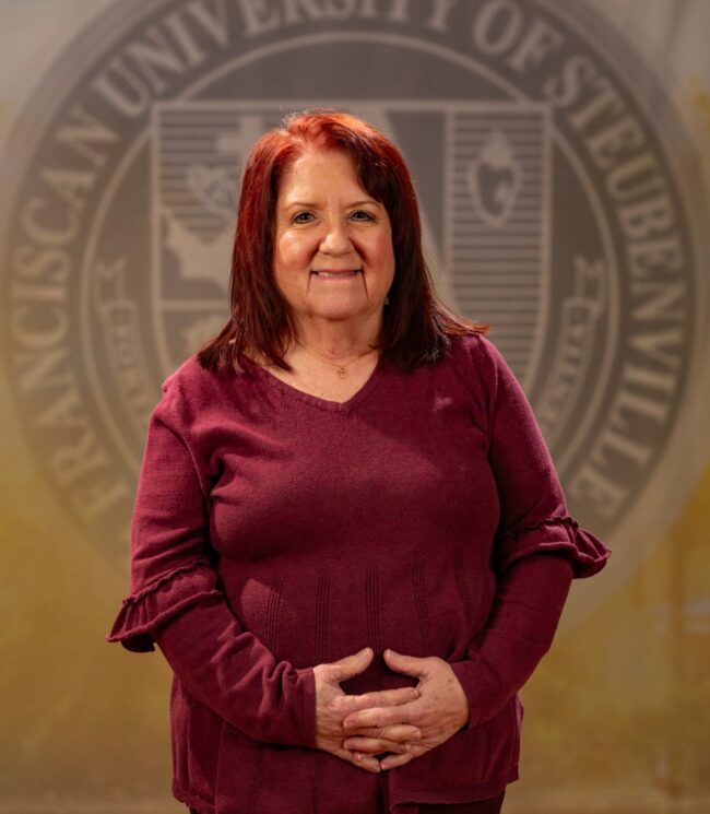 Faculty portrait of Dr. Kimberley Donnelly standing in front of the Franciscan University of Steubenville seal.